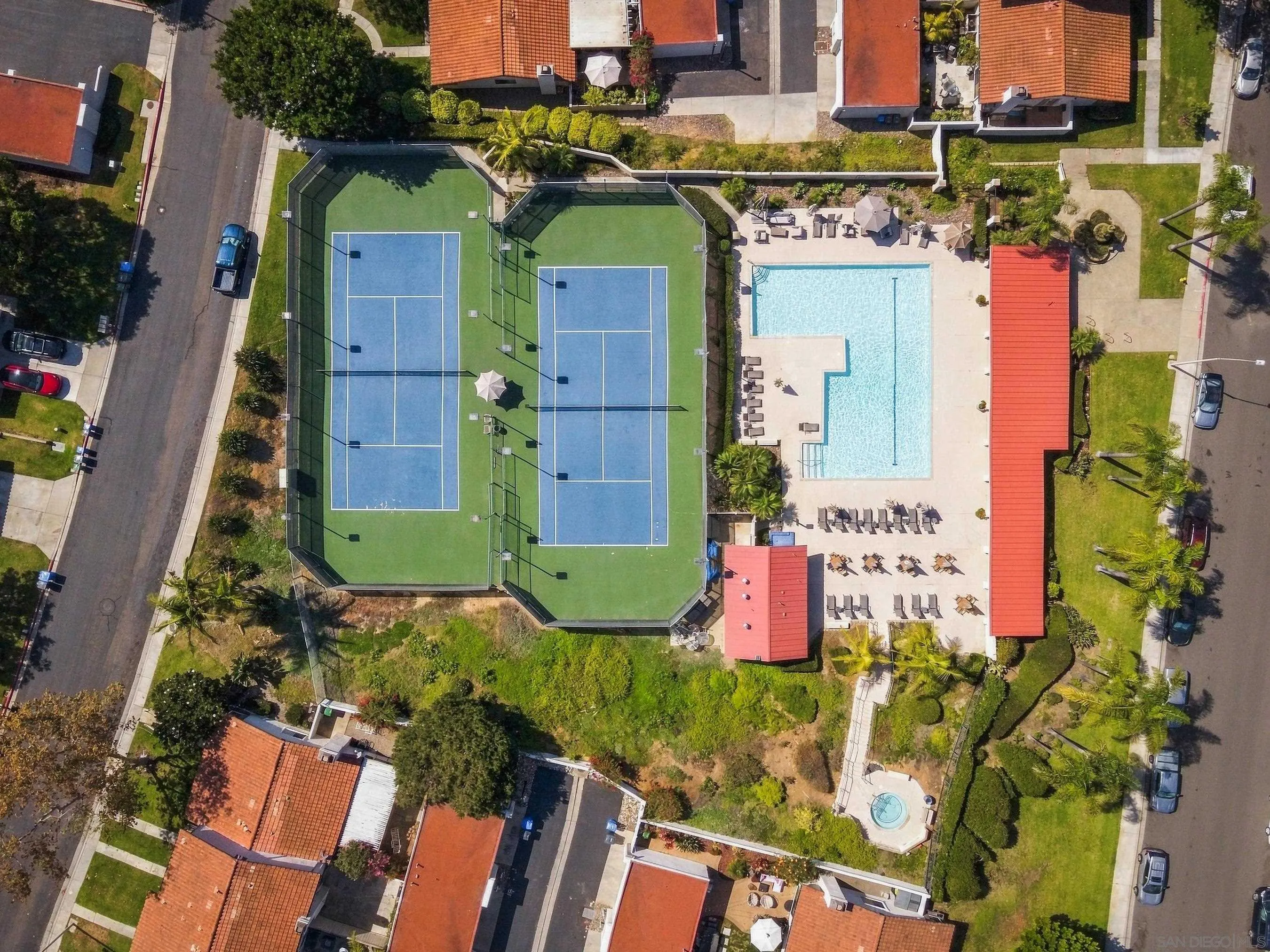 Aerial view of a community with two tennis courts beside a pool and landscaped grounds.