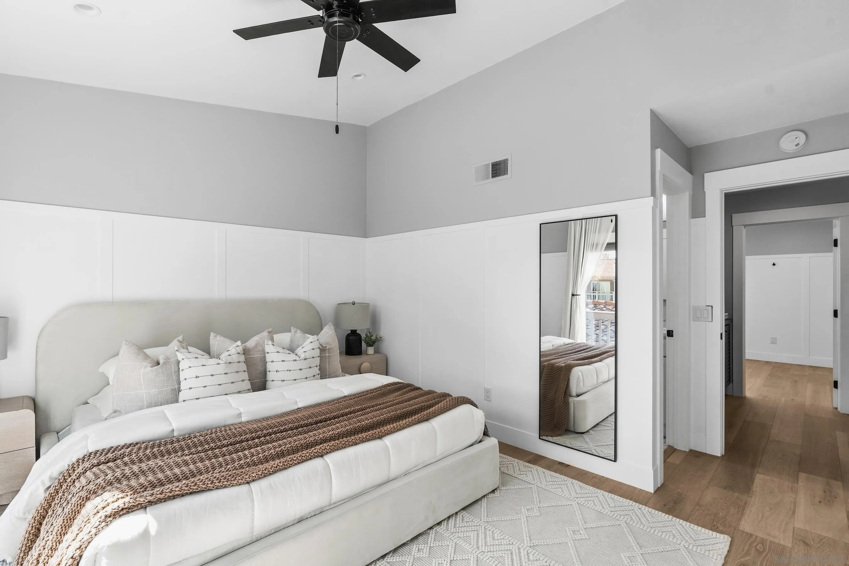 Staged bedroom with an upholstered bed, brown knit throw, paneled walls, and a black ceiling fan.