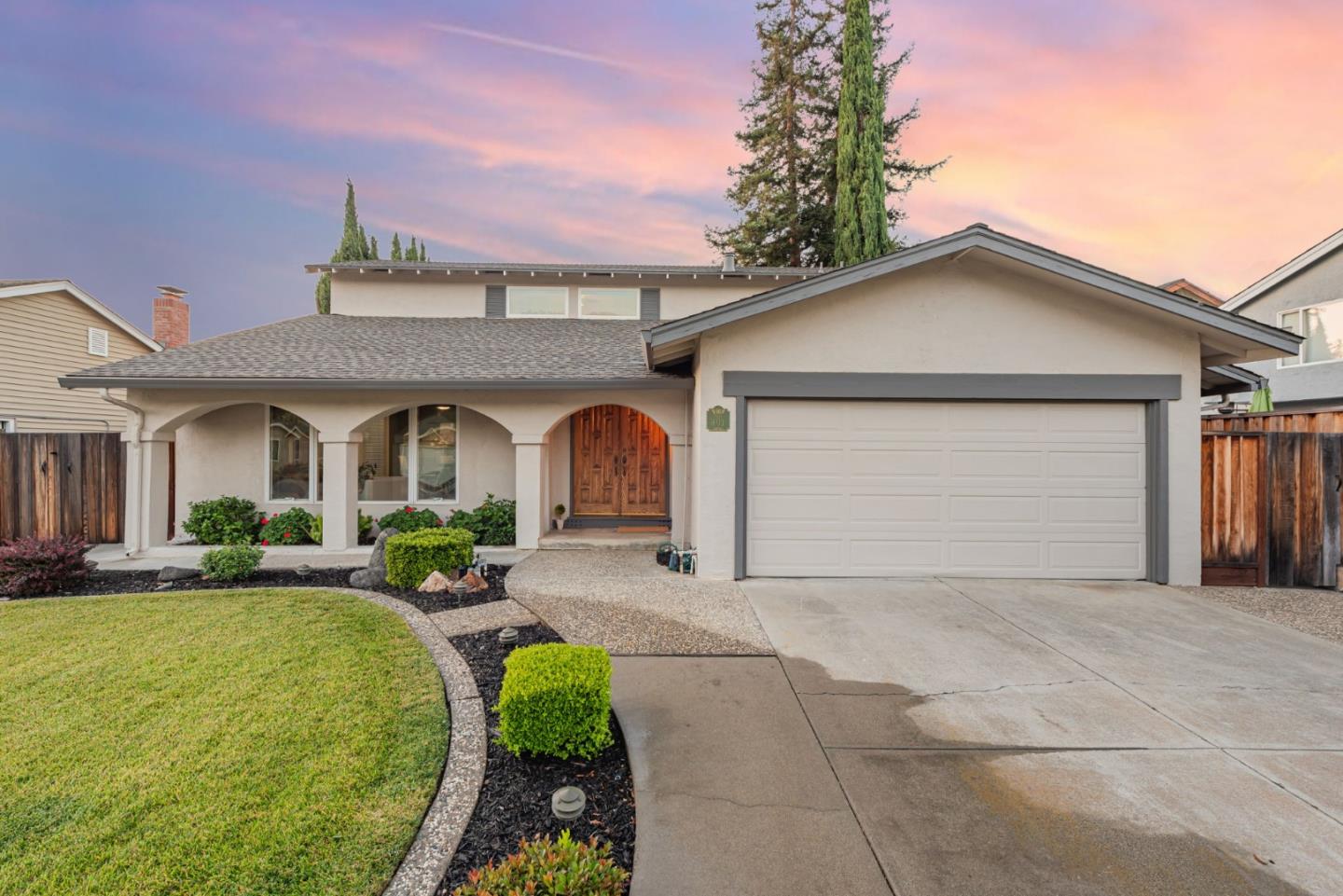 Single-story home with an attached two-car garage, arched porch, and landscaped front yard at dusk.