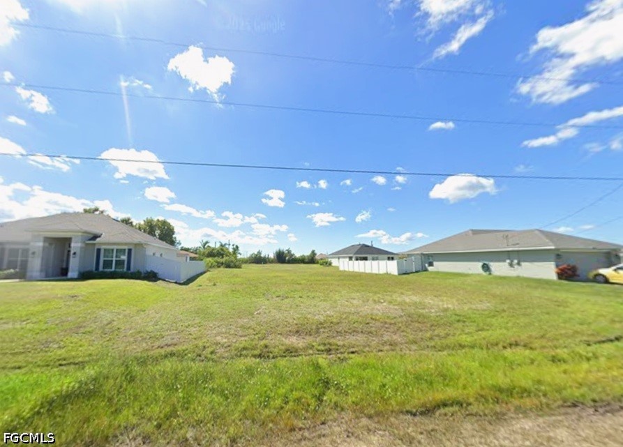 Grassy vacant lot between single-story homes beneath a bright blue sky.