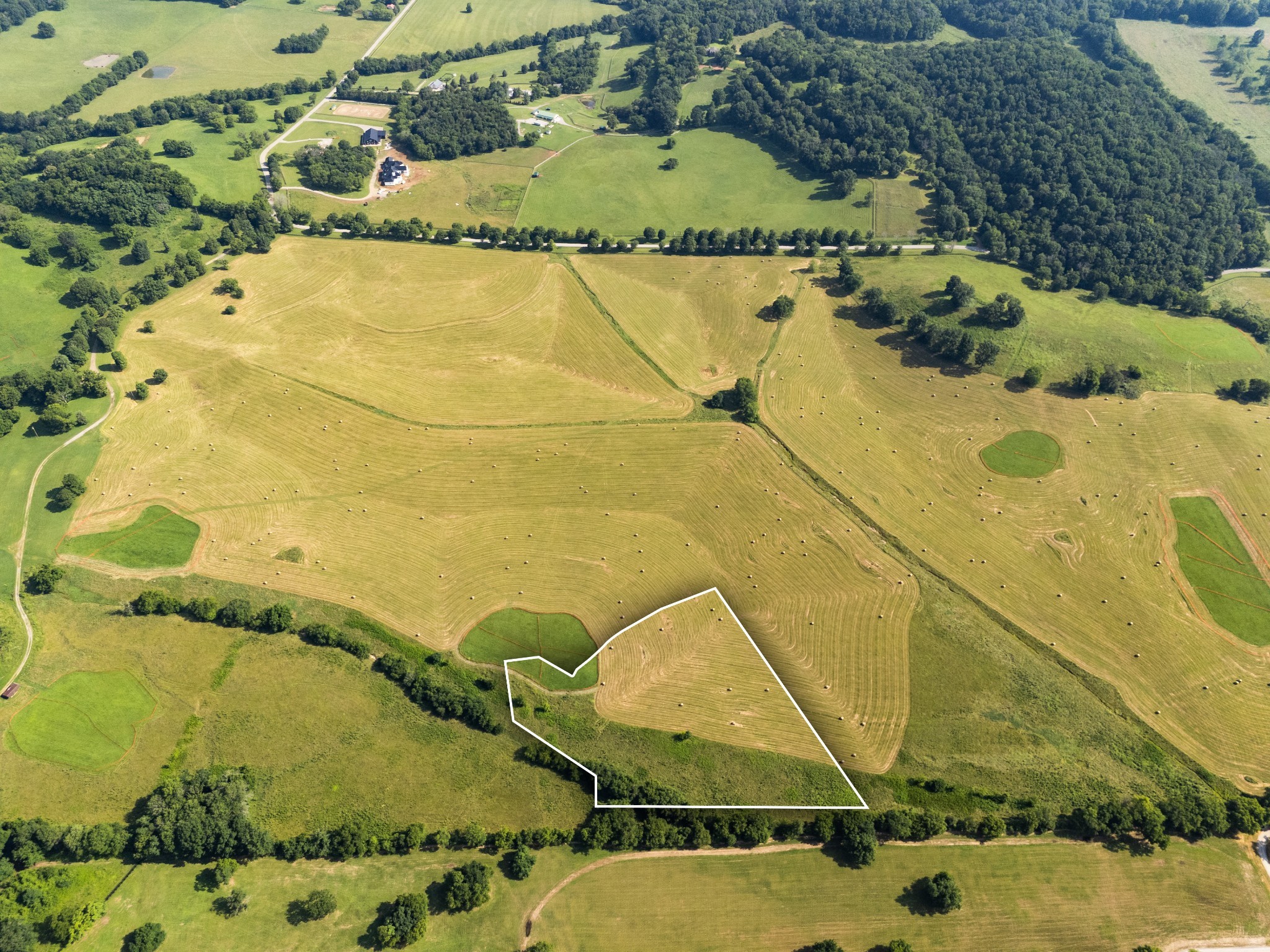 Aerial view of a marked rural parcel amid hay fields and wooded boundaries.