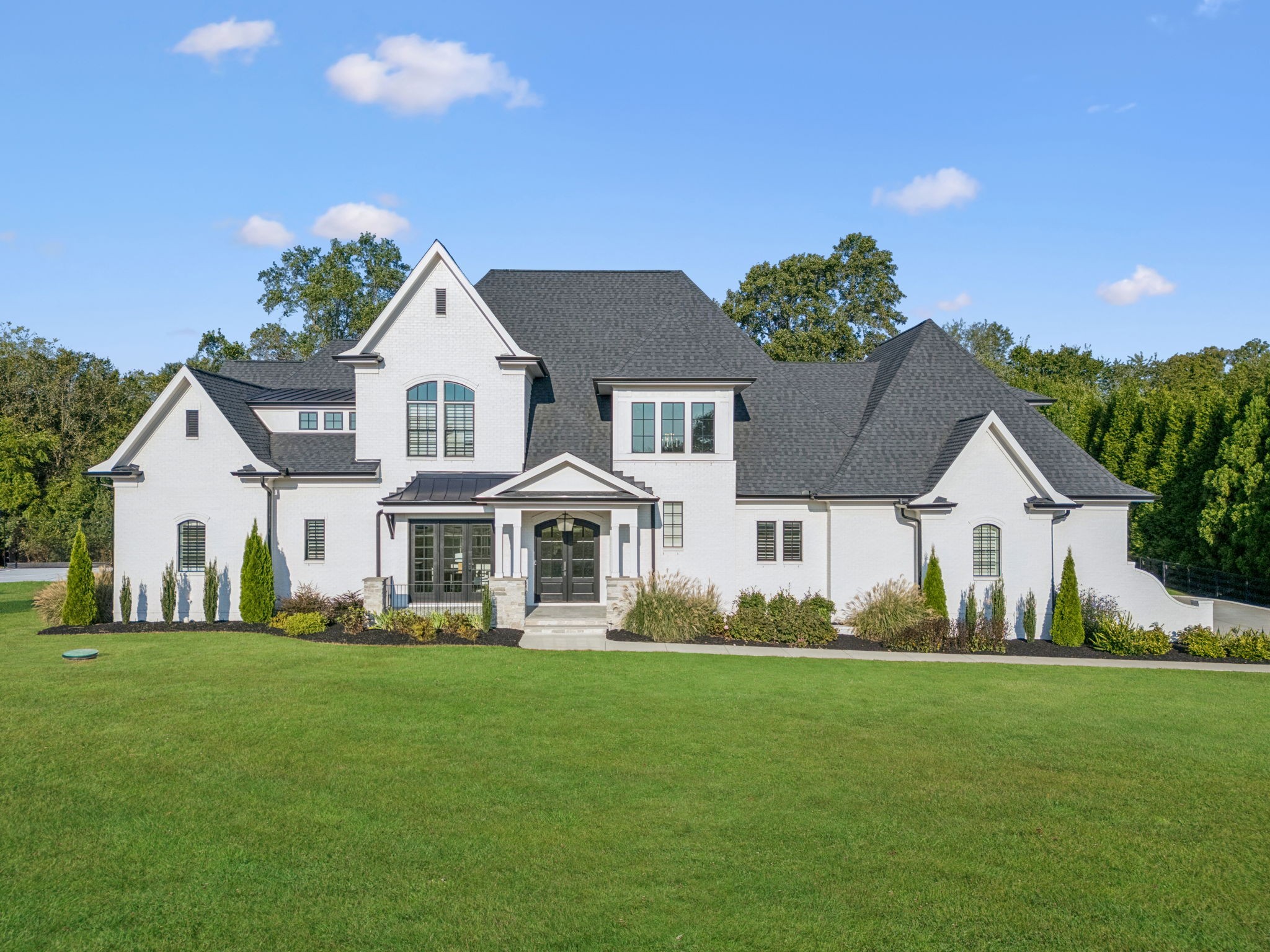 White two-story house with a dark gabled roof, covered entrance, landscaped beds, and broad lawn.