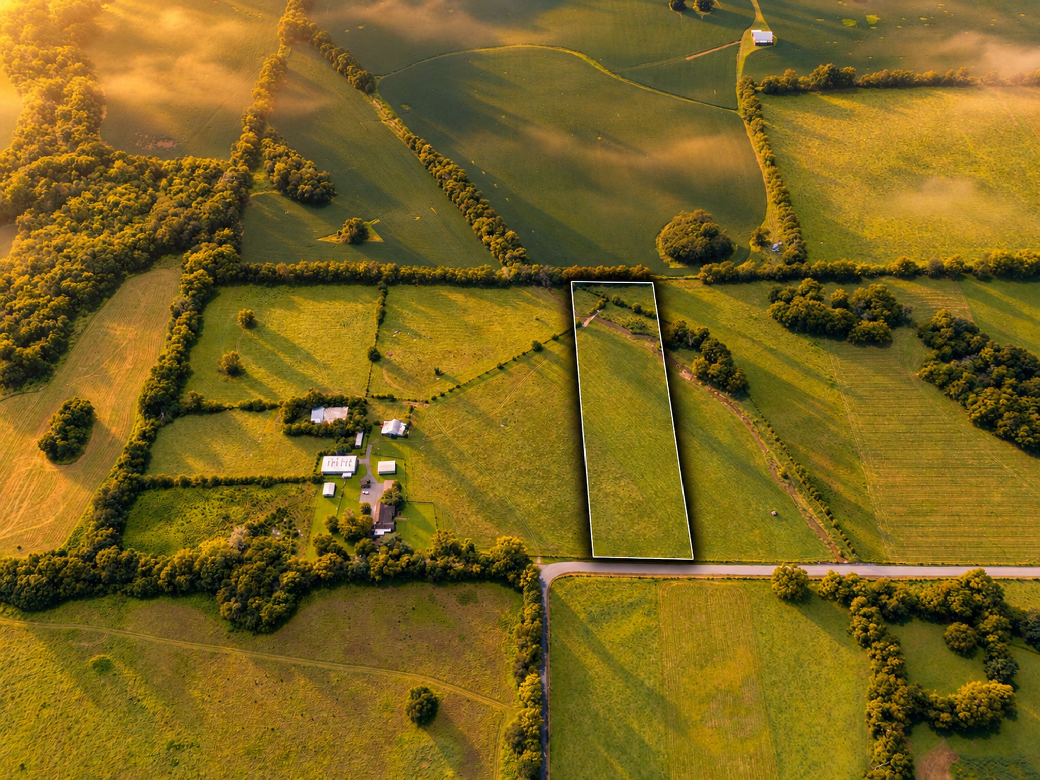 Aerial view of a long, white-outlined rural parcel bordered by fields and a road.