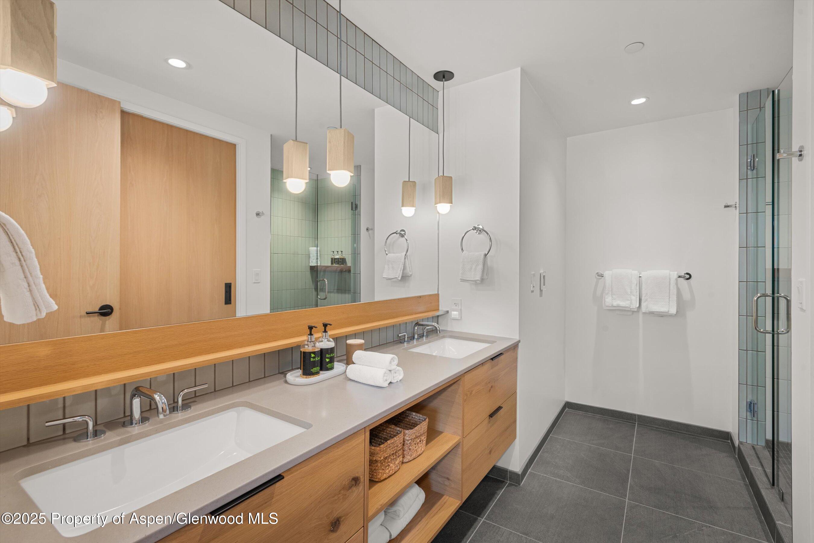 Modern bathroom with a long double-sink wood vanity and glass-enclosed tiled shower.