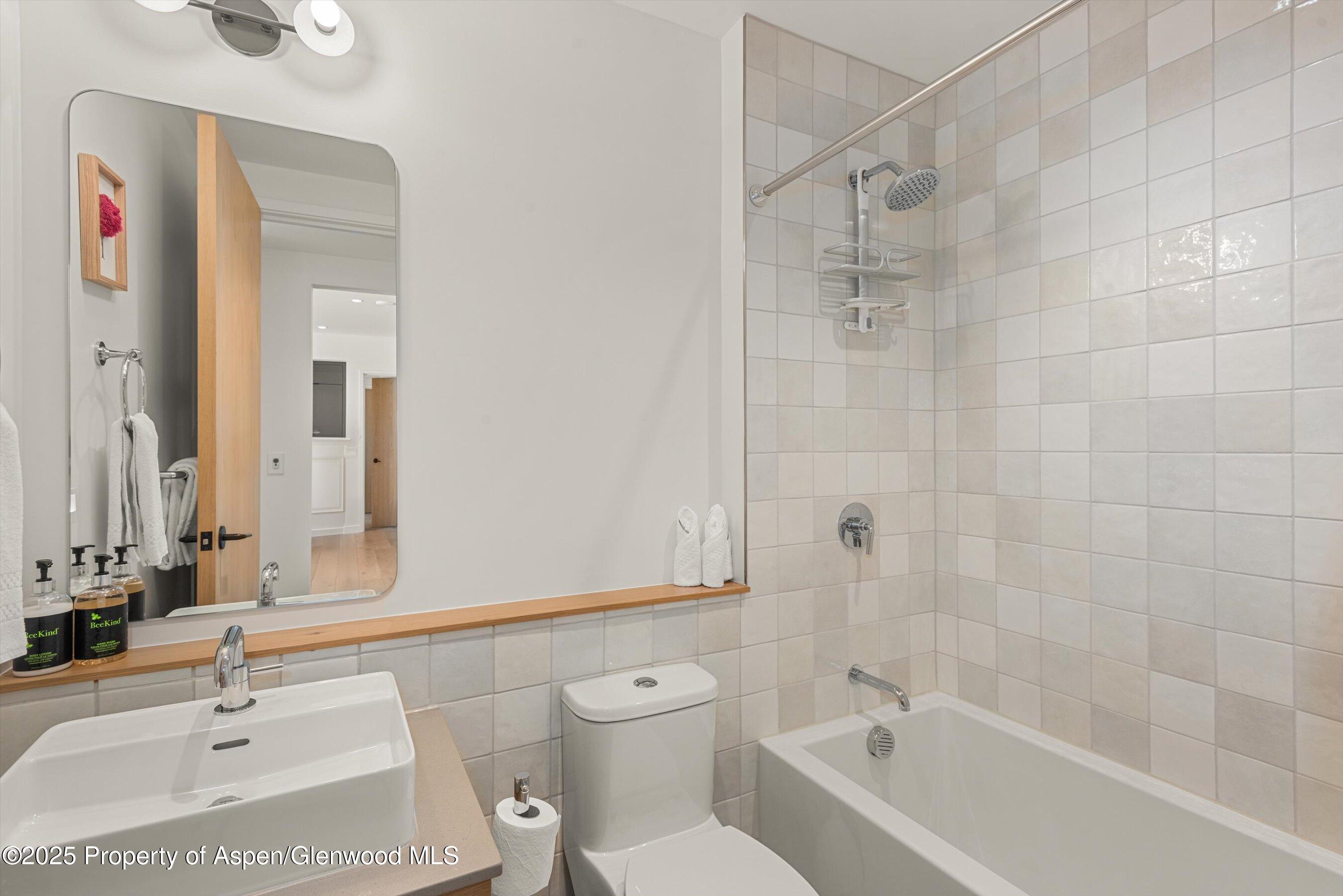 Bathroom with a tiled tub and shower, vessel sink, and large mirror.