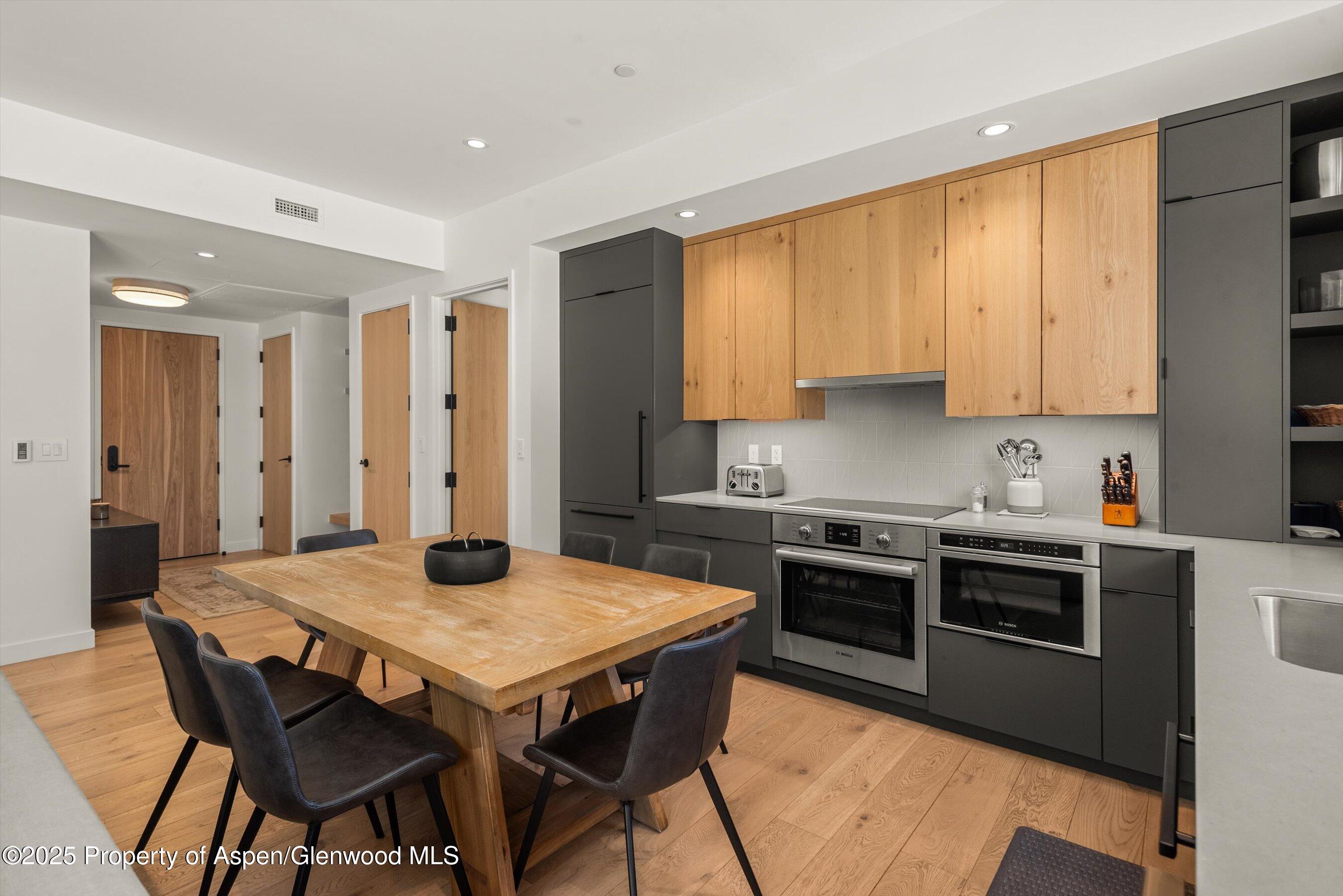 Modern kitchen with wood cabinets, double ovens, and a large dining table with dark chairs.