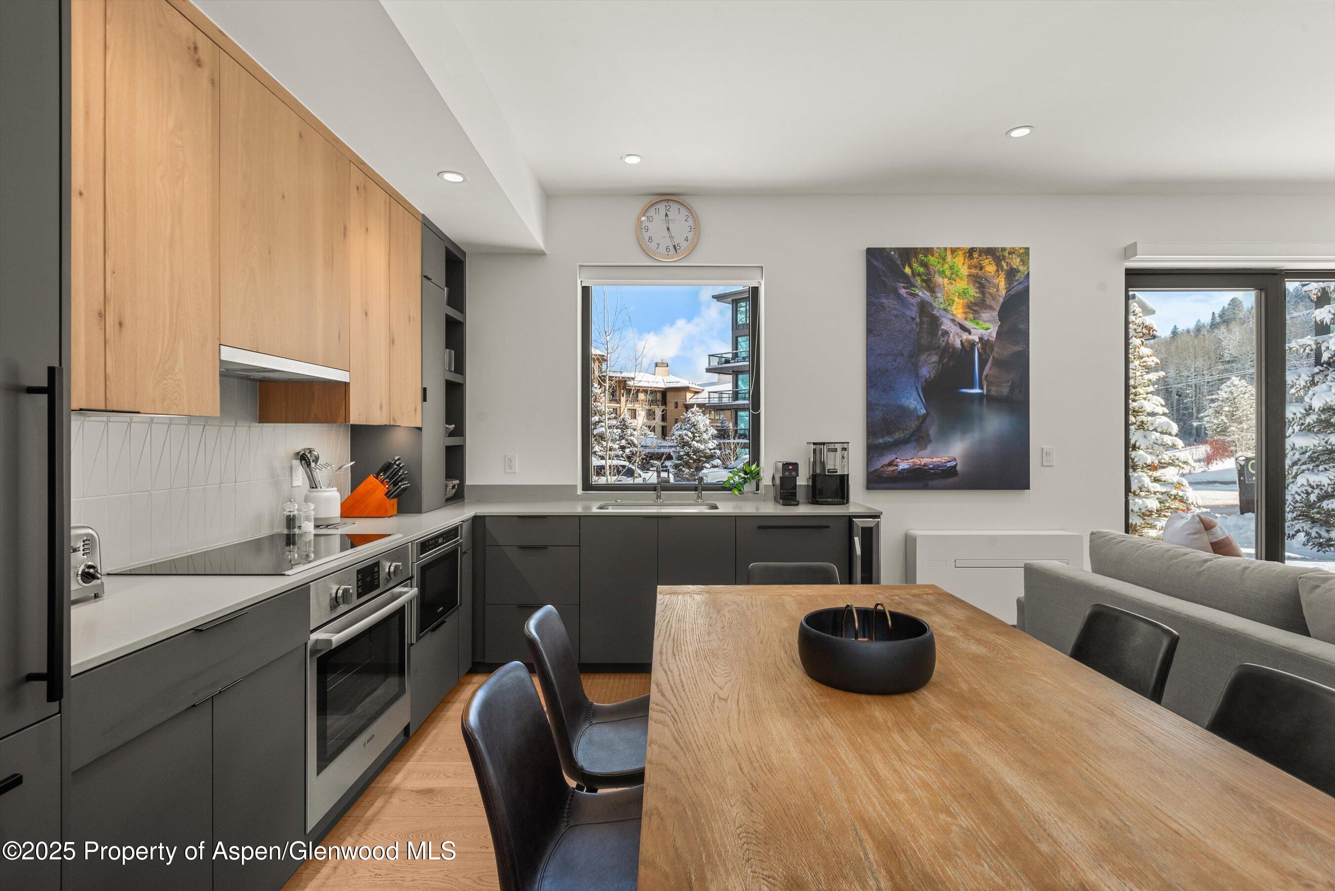 Modern kitchen and dining area with wood cabinetry, a large dining table, and snowy views through the windows.