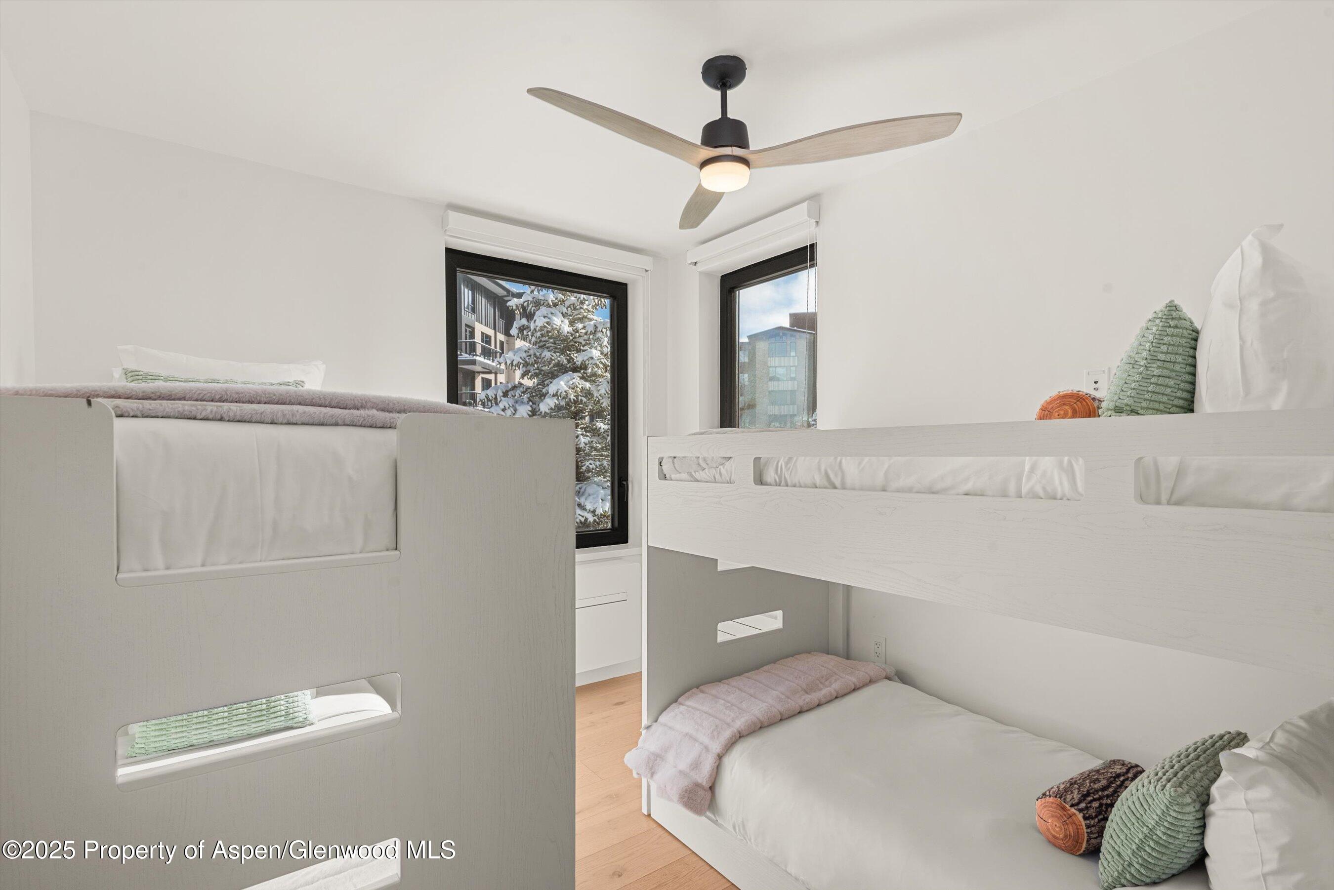 Bright bedroom with white built-in bunk beds and snowy trees visible through the windows.