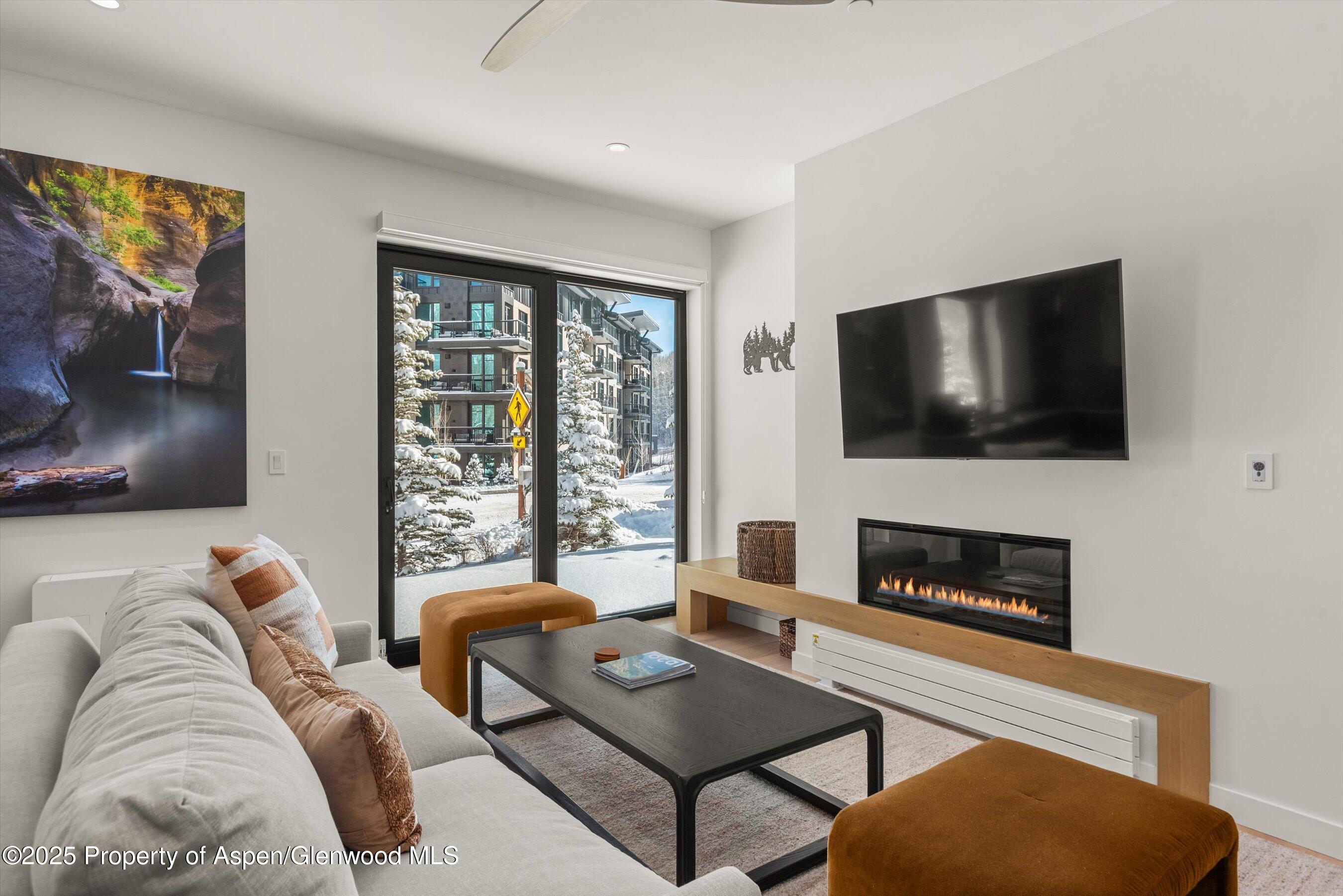 Living room with a linear fireplace and sliding glass doors overlooking a snowy courtyard.