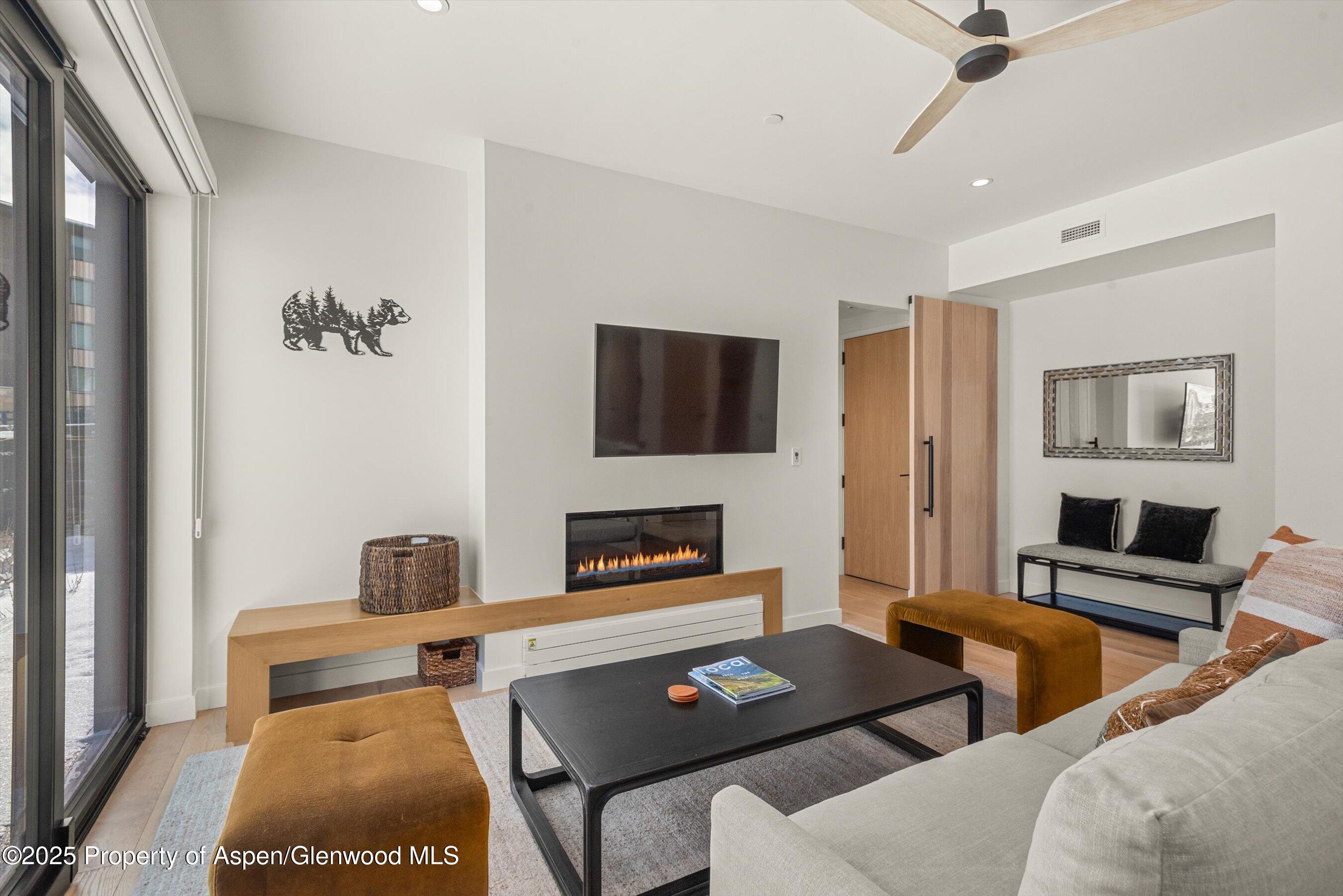 Modern living room with a linear fireplace, wall-mounted television, and large sliding glass doors.