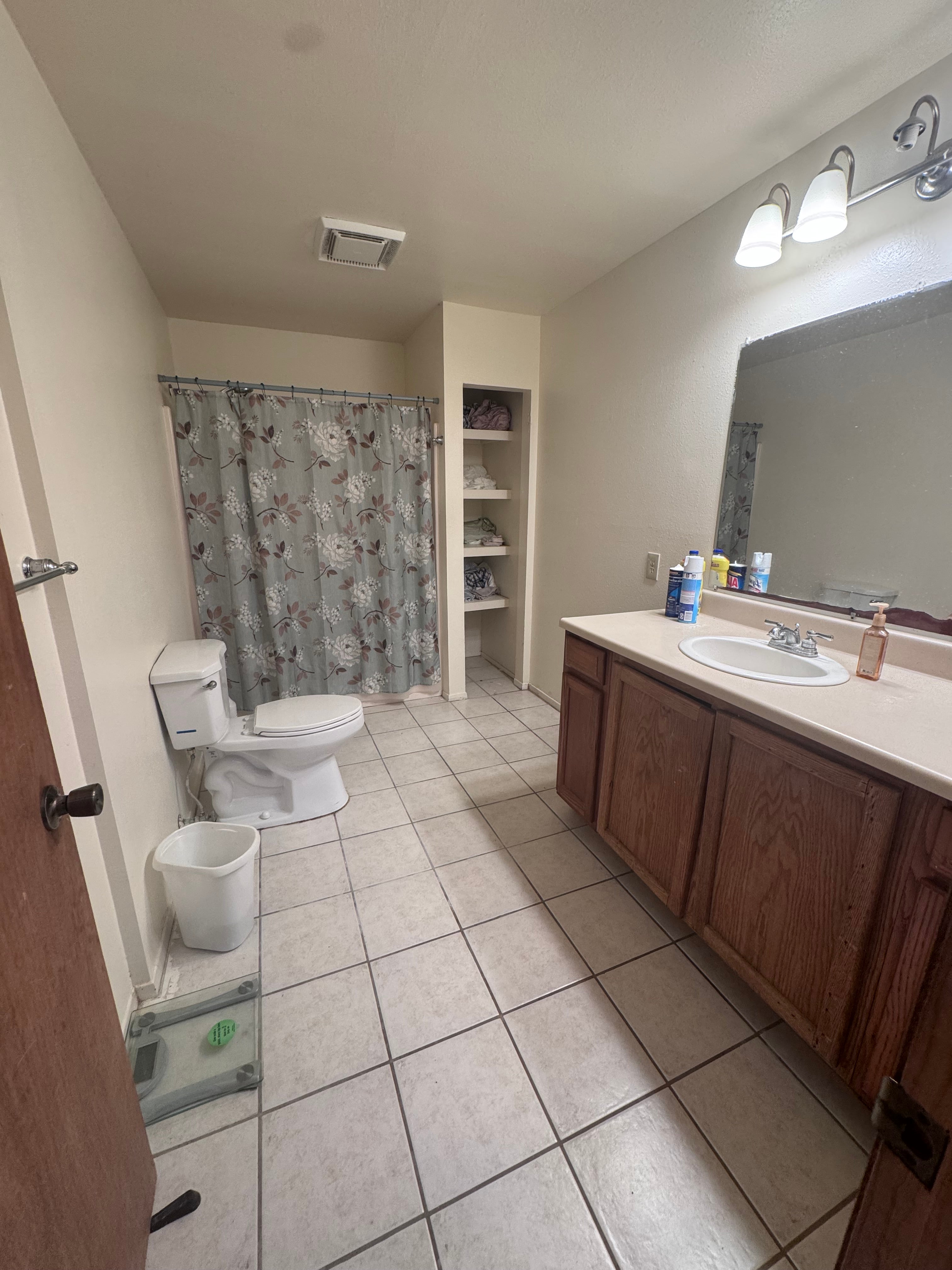 Bathroom with a wood vanity, tiled floor, toilet, and floral shower curtain.