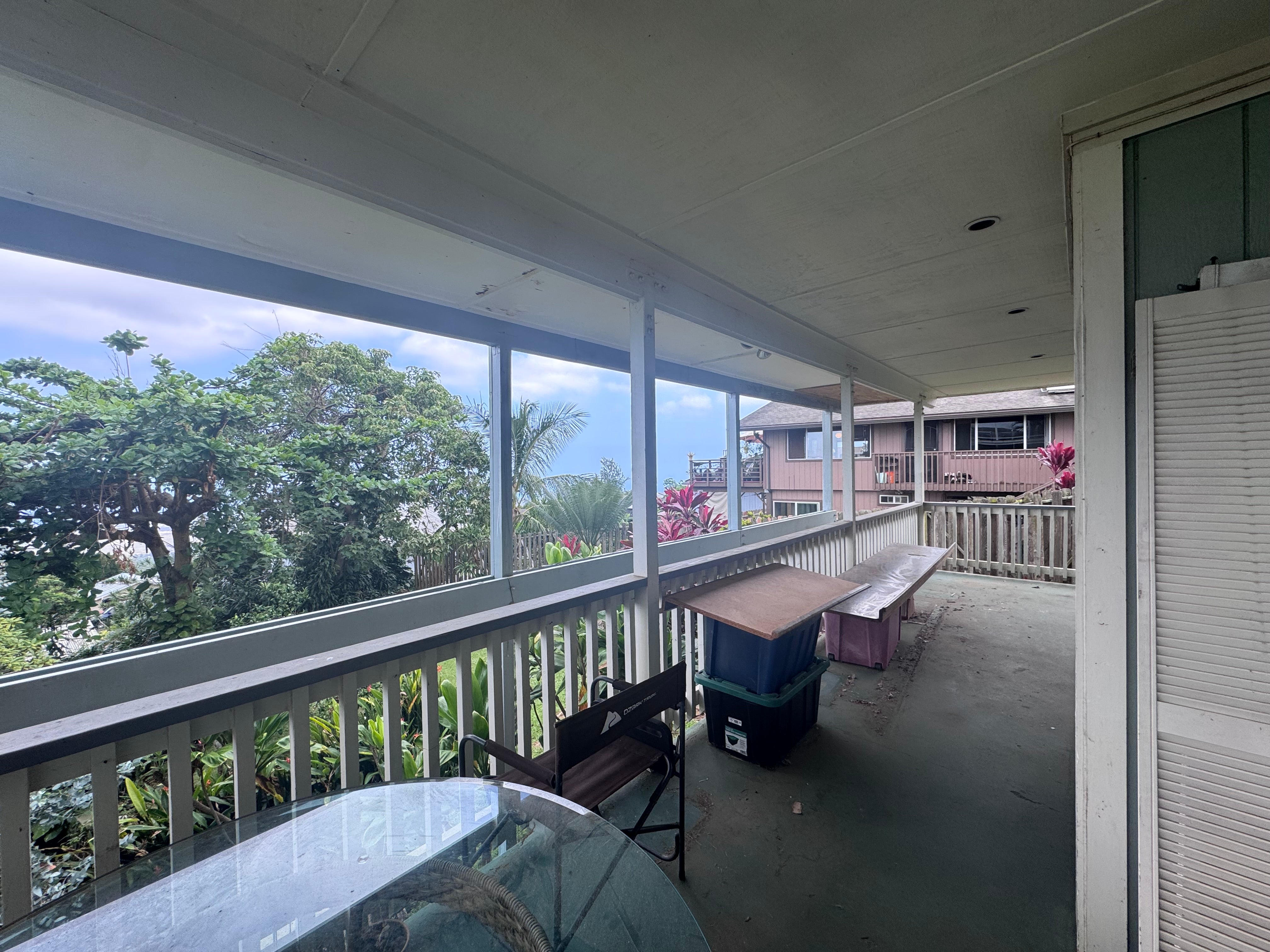 Covered lanai with white railings, outdoor seating, tropical foliage, and a neighboring home.