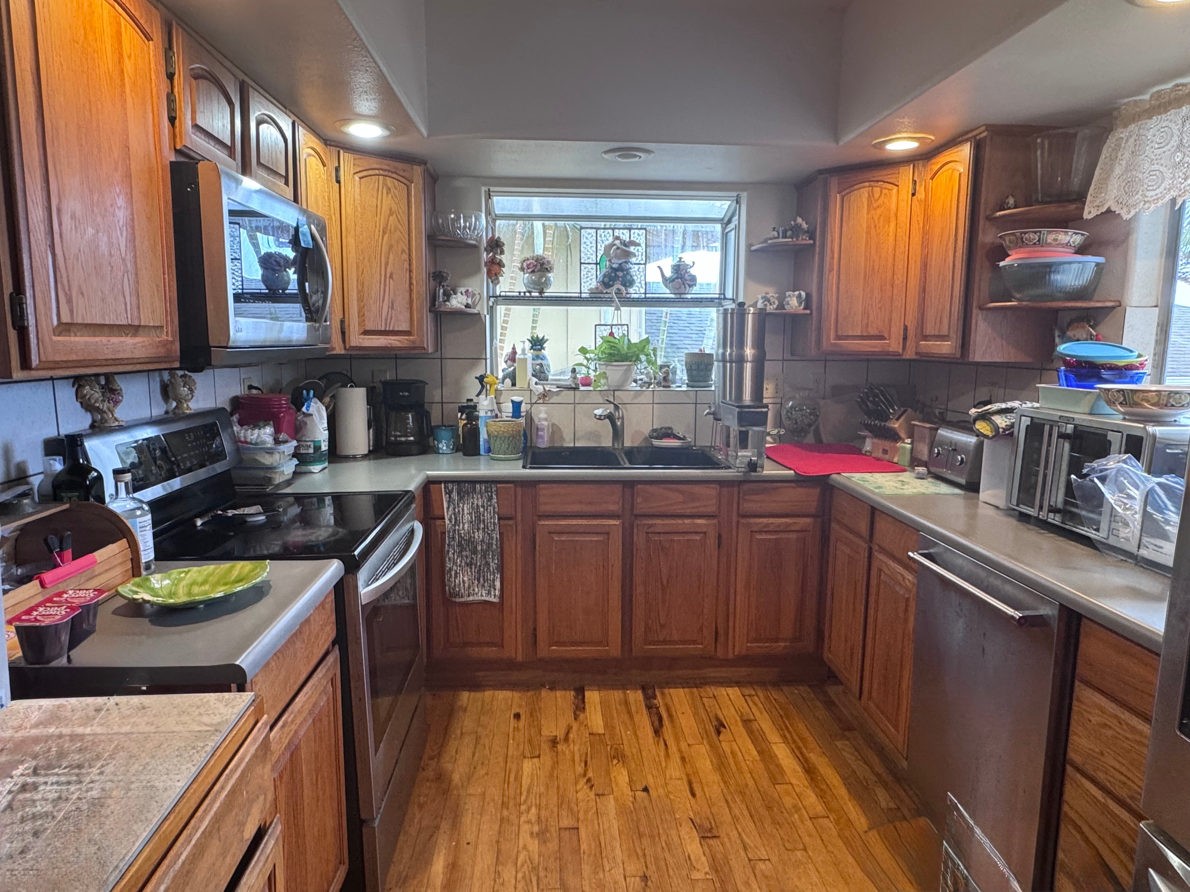 Kitchen with wood cabinets and plank flooring, a sink below a window, and stainless steel appliances.