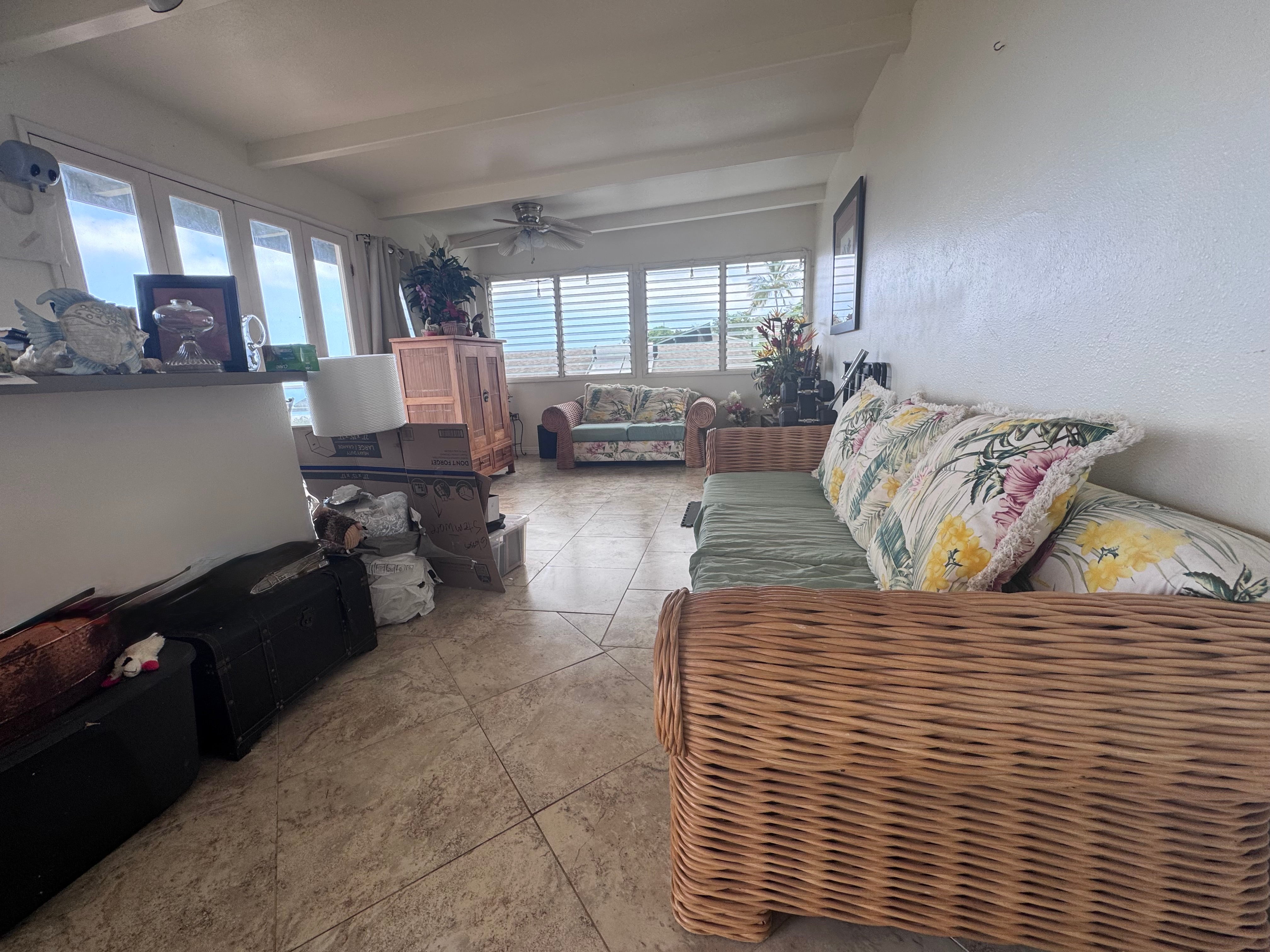 Living room with wicker seating, tropical floral cushions, and louvered windows facing the ocean.