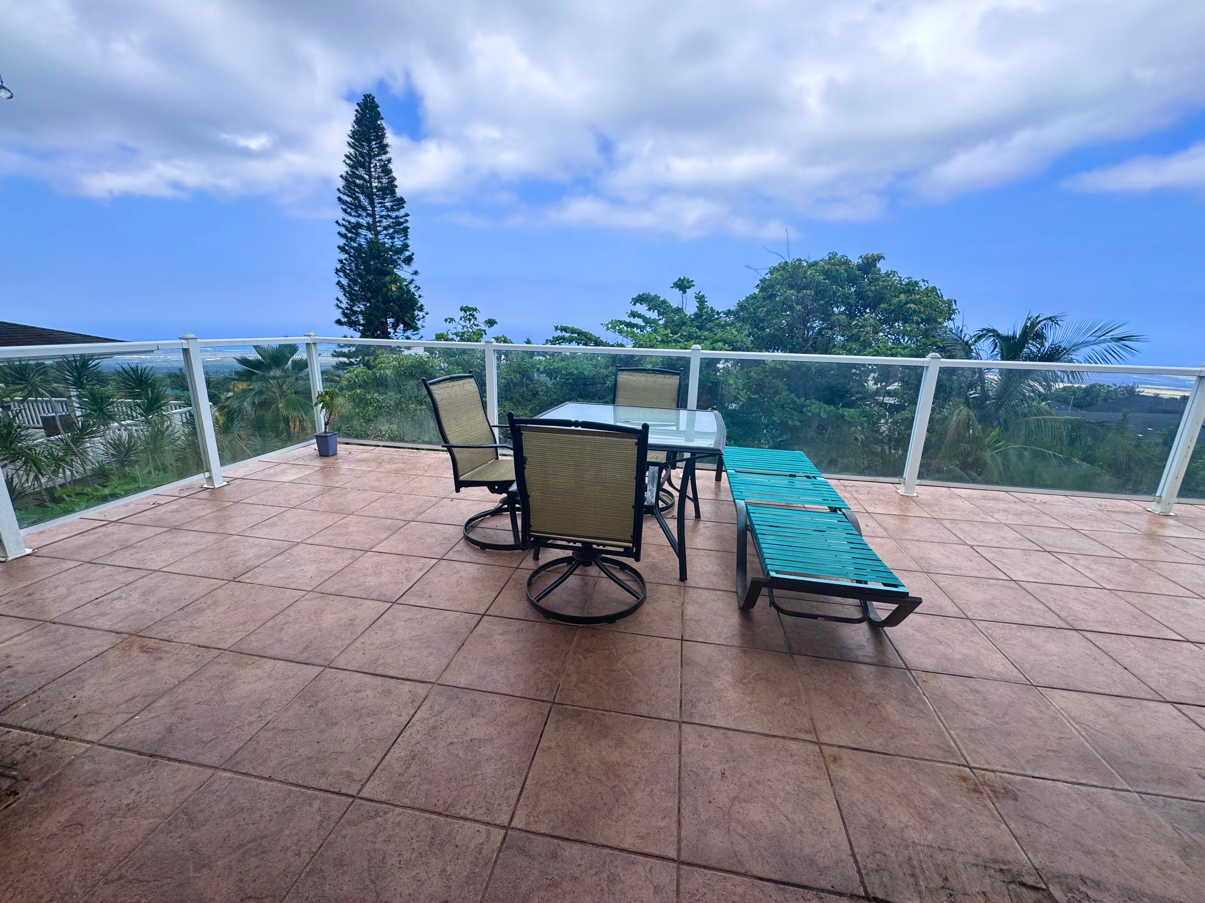 Tiled terrace with dining furniture and a turquoise chaise lounge overlooking the ocean.