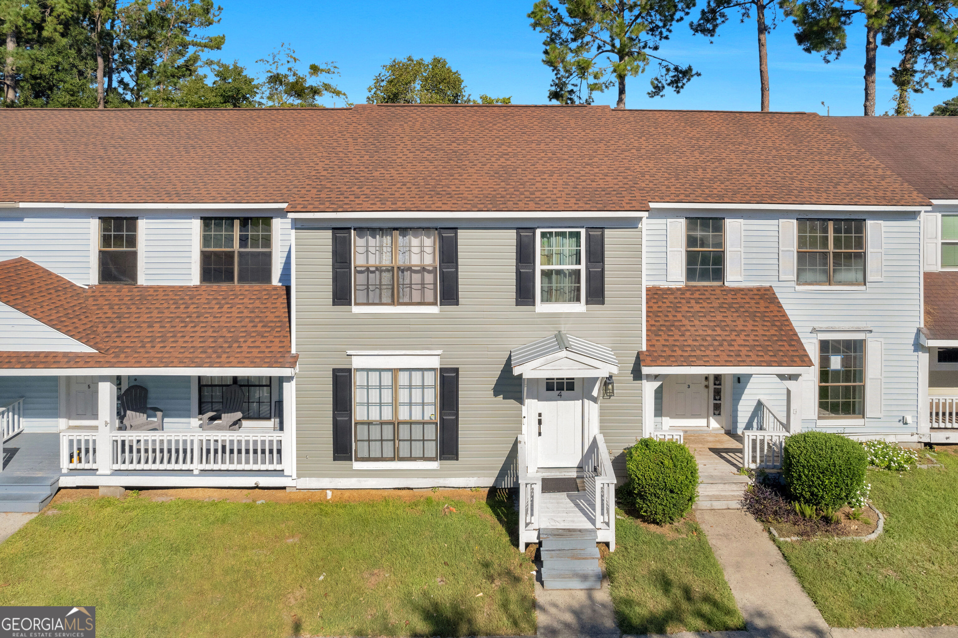 Two-story attached home with gray siding, a brown shingle roof, and a white front porch.