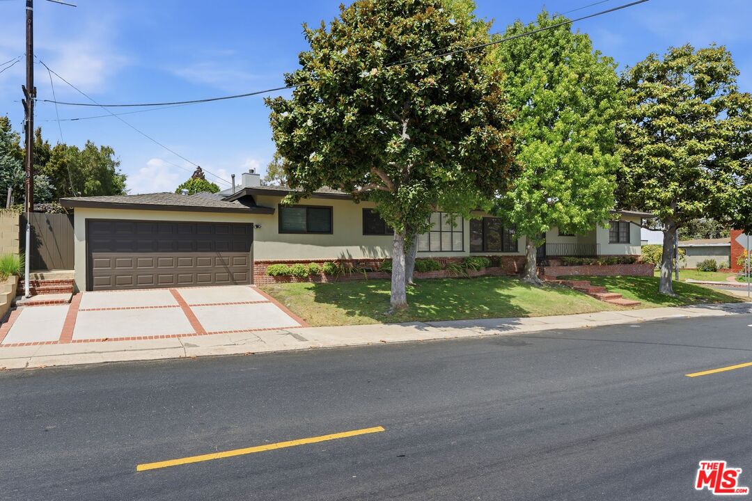 Single-story house with a wide double garage and mature trees shading the front lawn.
