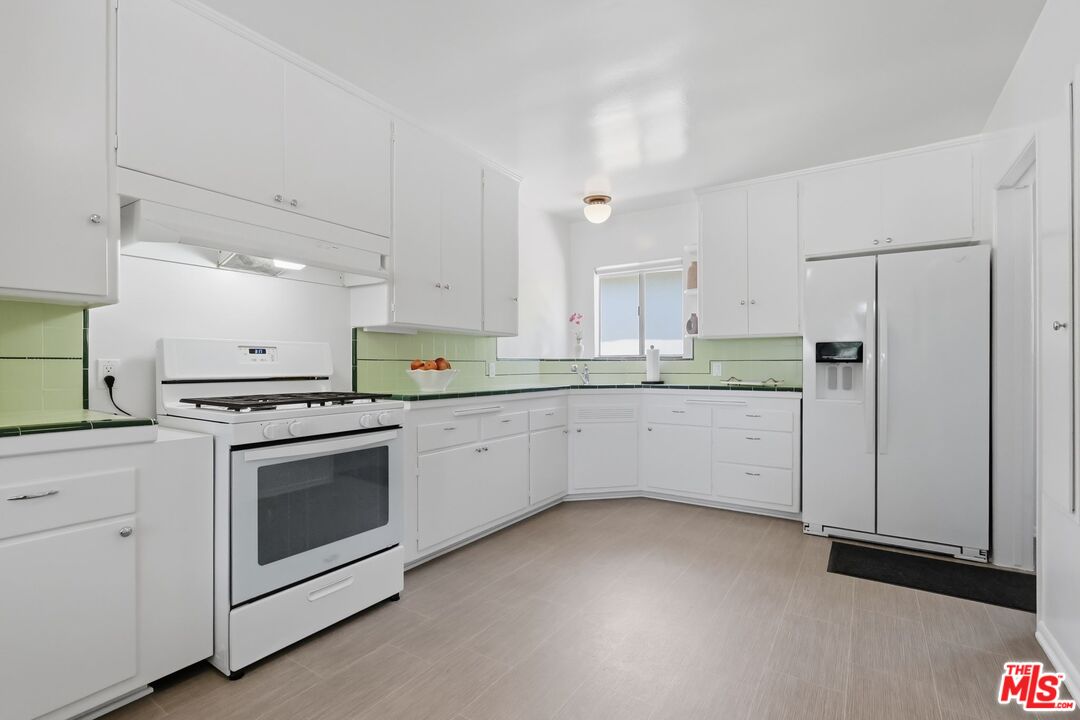Kitchen with white cabinets, pale green backsplash, gas range, and side-by-side refrigerator.
