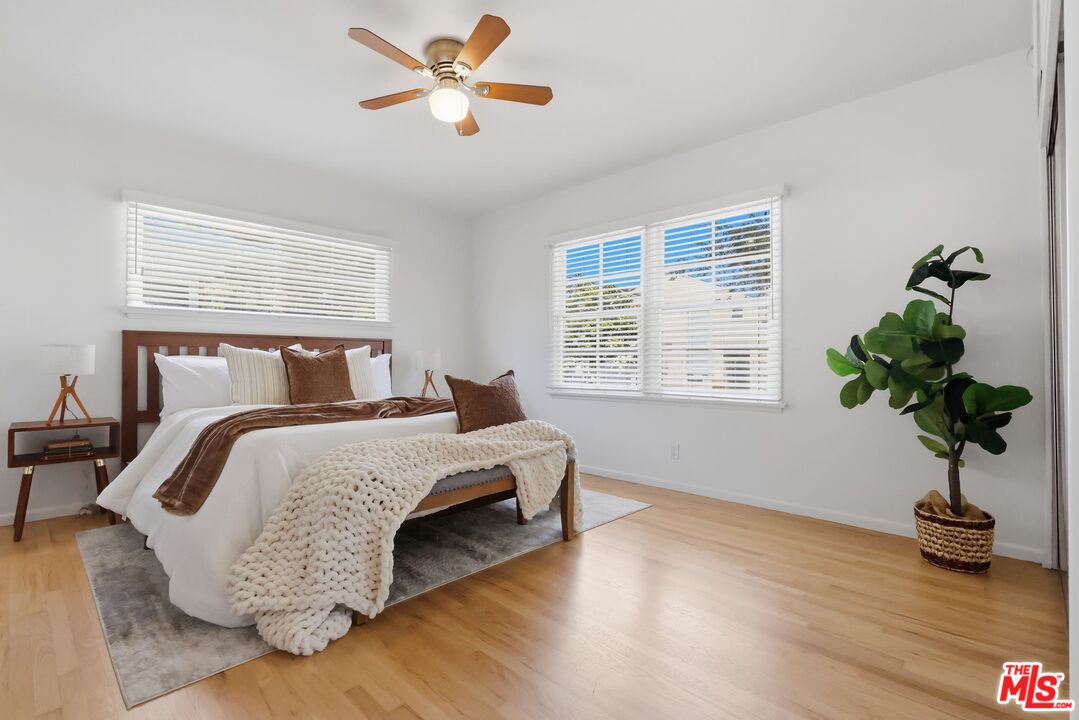 Staged bedroom with a wooden bed, chunky knit blanket, hardwood floors, and shuttered windows.