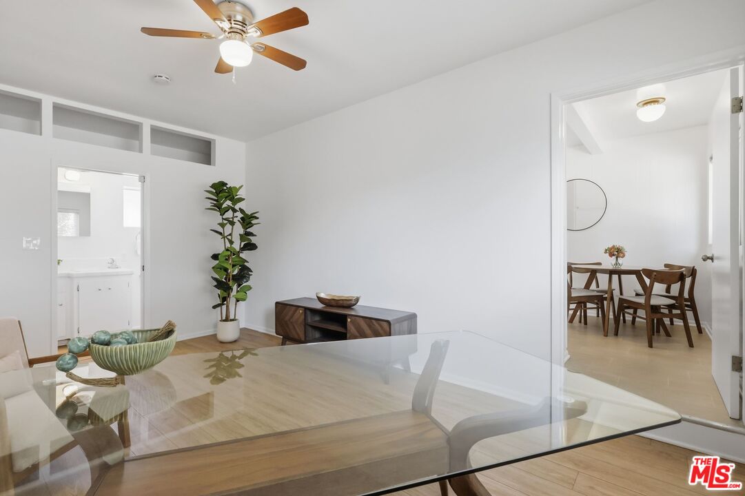 Dining area with a glass-top table, wood ceiling fan, and adjacent room with a wooden dining set.