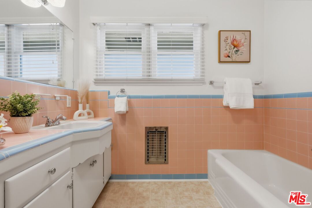 Bathroom with peach-pink tile, blue trim, a white bathtub, and a white vanity.