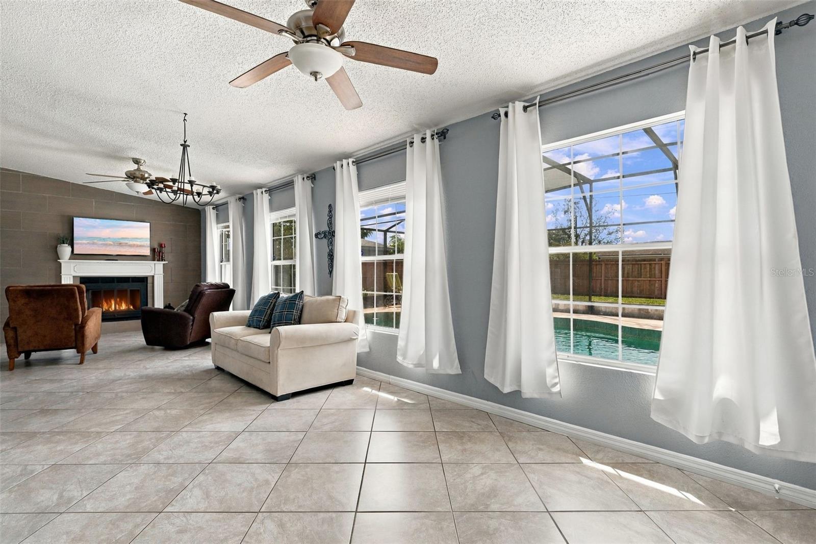 Furnished living room with a fireplace and large windows overlooking a backyard pool.
