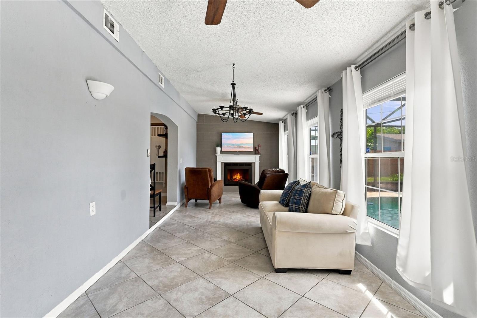 Living room with tiled floors, a fireplace, and windows overlooking a pool.