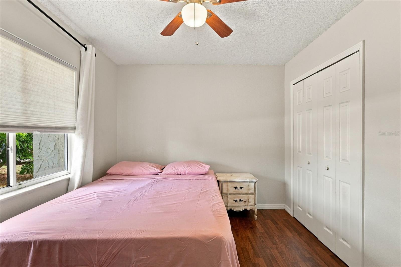 Bedroom with a pink bed, ceiling fan, and white closet doors.