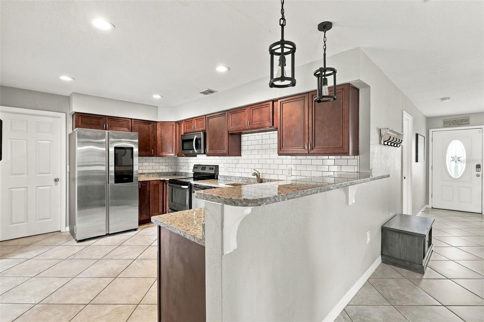 Kitchen with dark wood cabinets, granite counters, stainless steel appliances, and a raised breakfast bar.