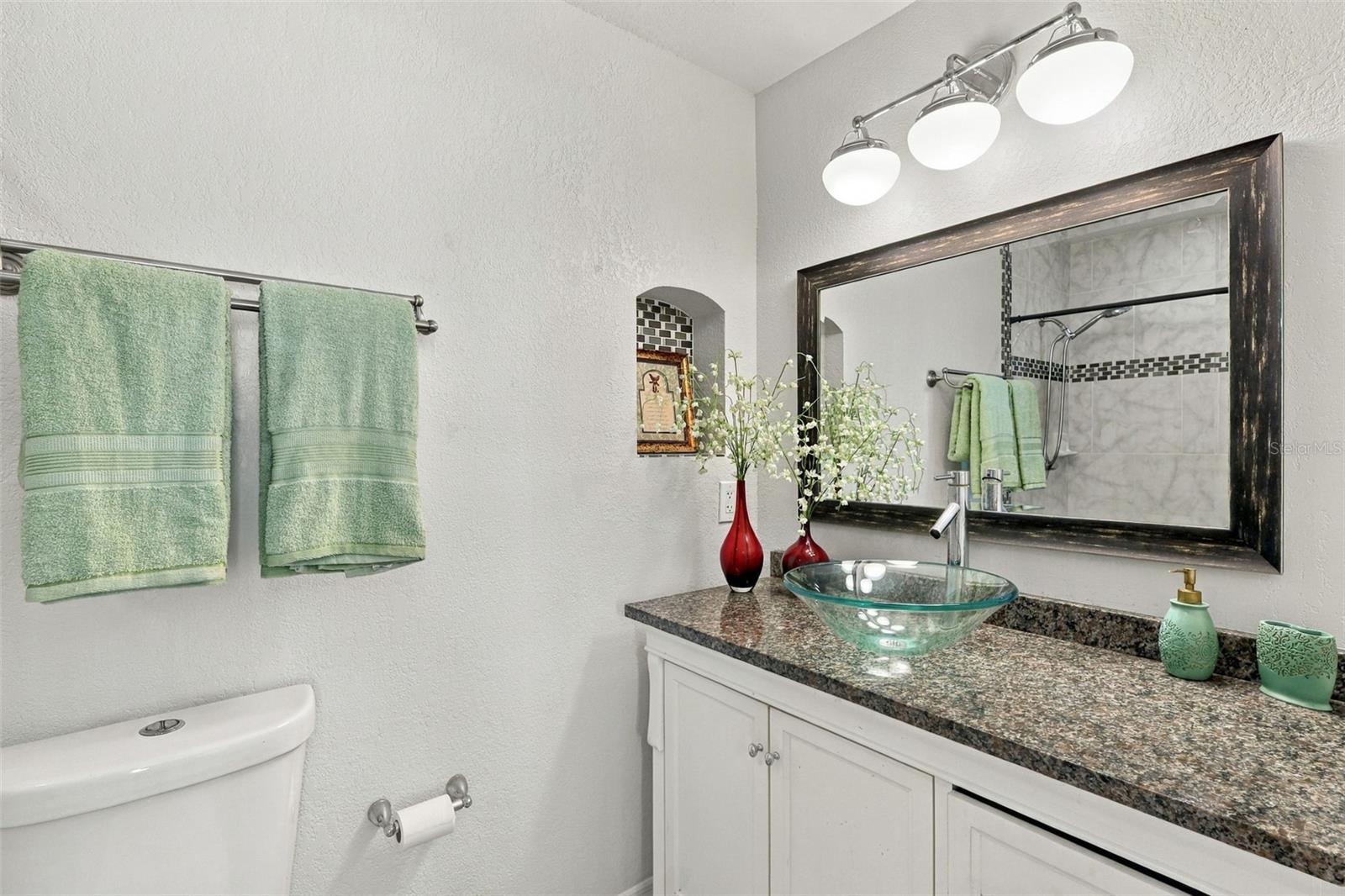 Bathroom vanity with a glass vessel sink, speckled countertop, and large dark-framed mirror.