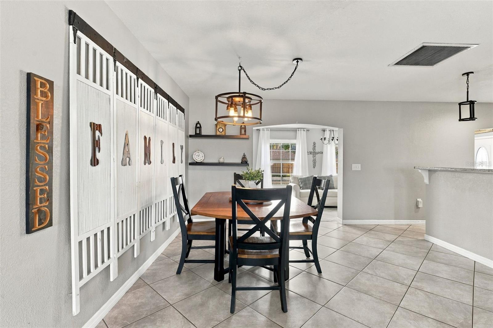 Dining room with a wooden table, black chairs, tiled floor, and FAMILY wall decor.