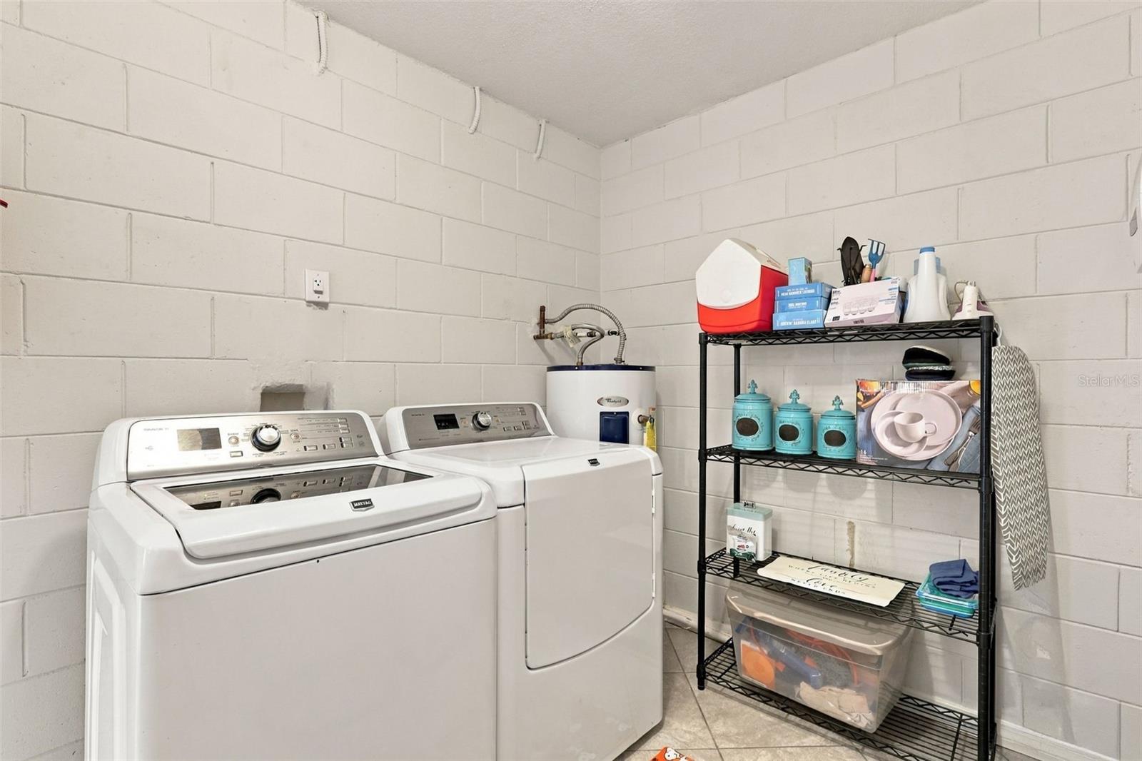 Laundry room with a white washer and dryer beside a black storage shelf.