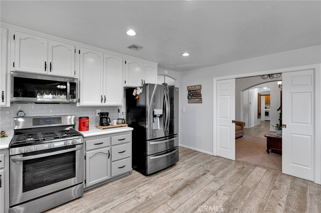 Kitchen with white cabinets, stainless steel appliances, and gray wood-look flooring.