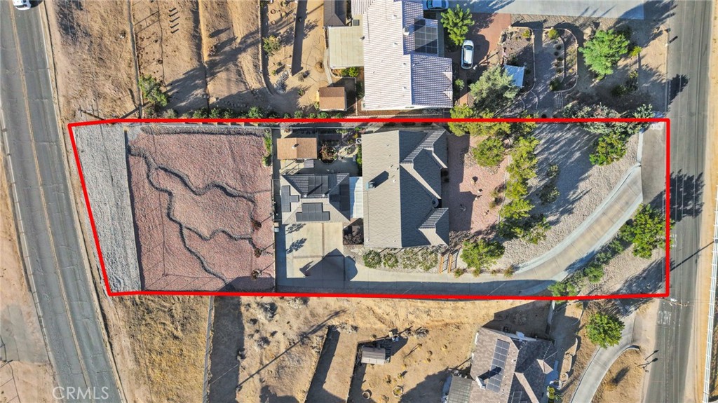 Aerial view of a single-story home and lot outlined in red, with a curved driveway and desert landscaping.