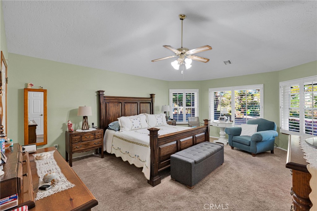 Furnished bedroom with a dark wood bed, gray bench, blue armchair, and shuttered windows.
