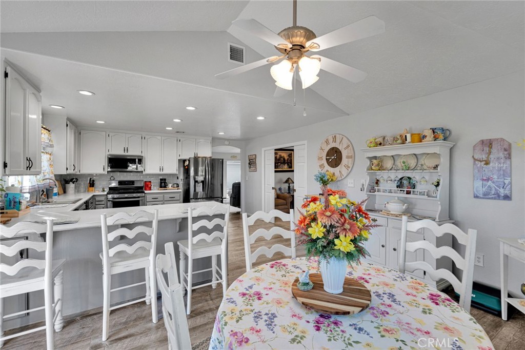 Open kitchen and dining area with a white breakfast bar, stainless appliances, and floral tablecloth.