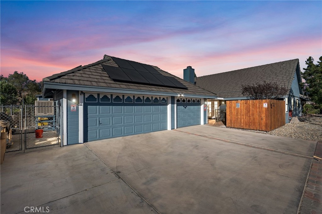 Blue-gray house with solar panels, a wide three-car garage, and a broad concrete driveway at dusk.