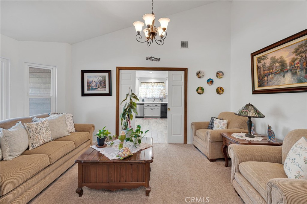 Living room with beige seating, a wooden coffee table, and a chandelier, opening to the kitchen.