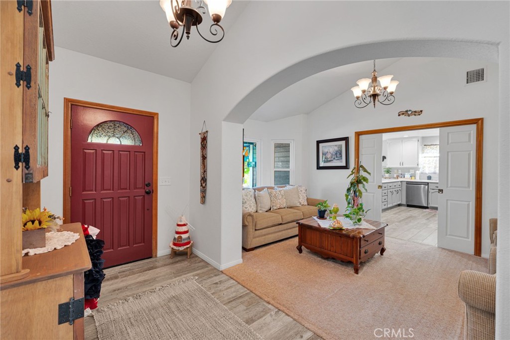 Entryway with a red front door opens to a furnished living room and bright white kitchen.
