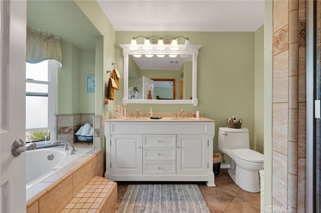 Bathroom with a white double vanity, tiled bathtub surround, and toilet.