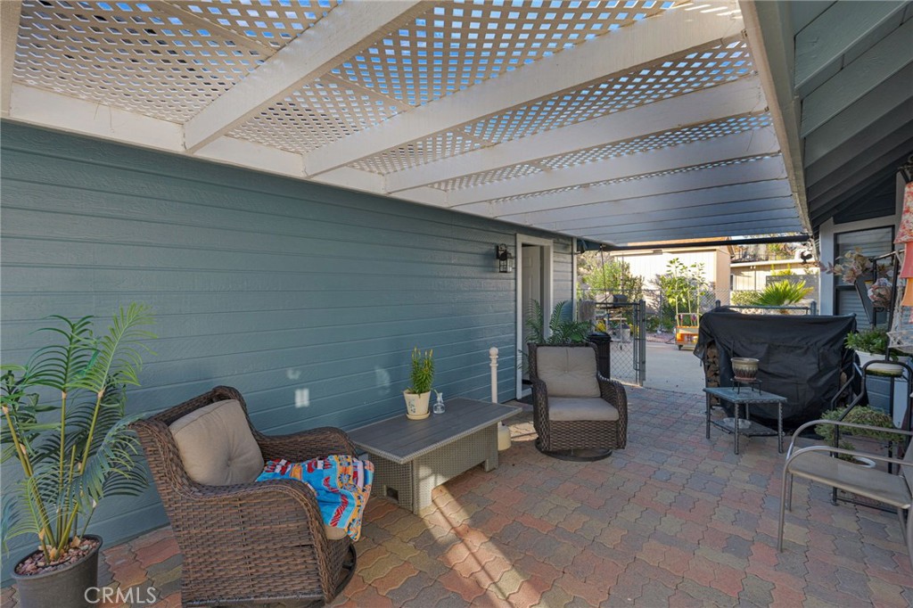 Covered patio with lattice pergola, paved floor, and wicker seating beside blue siding.