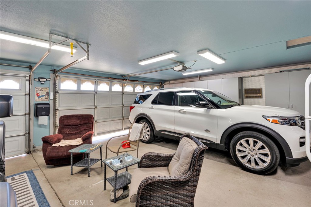 Garage with a white SUV parked beside a seating area with wicker chairs and a recliner.