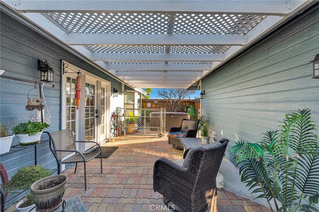 Covered patio with lattice pergola, patterned pavers, wicker seating, and potted plants.