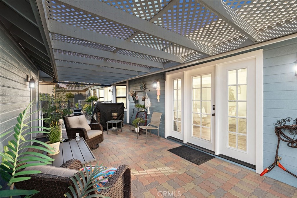 Covered patio with a white lattice pergola, French doors, brick pavers, and wicker seating.