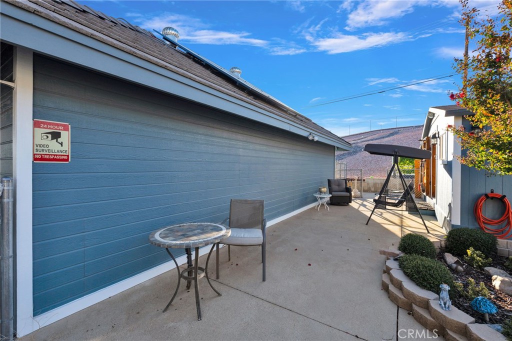 Concrete patio beside a blue-gray garage, with a covered swing and raised garden beds.