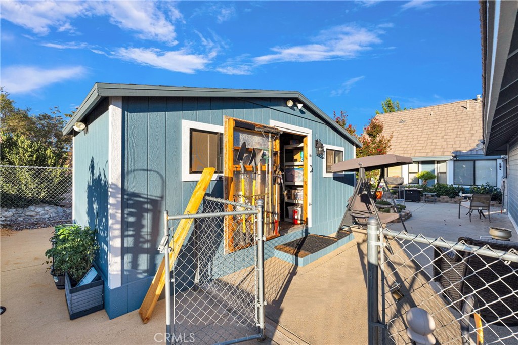 Blue backyard workshop with open doors, tools inside, and a fenced concrete patio.