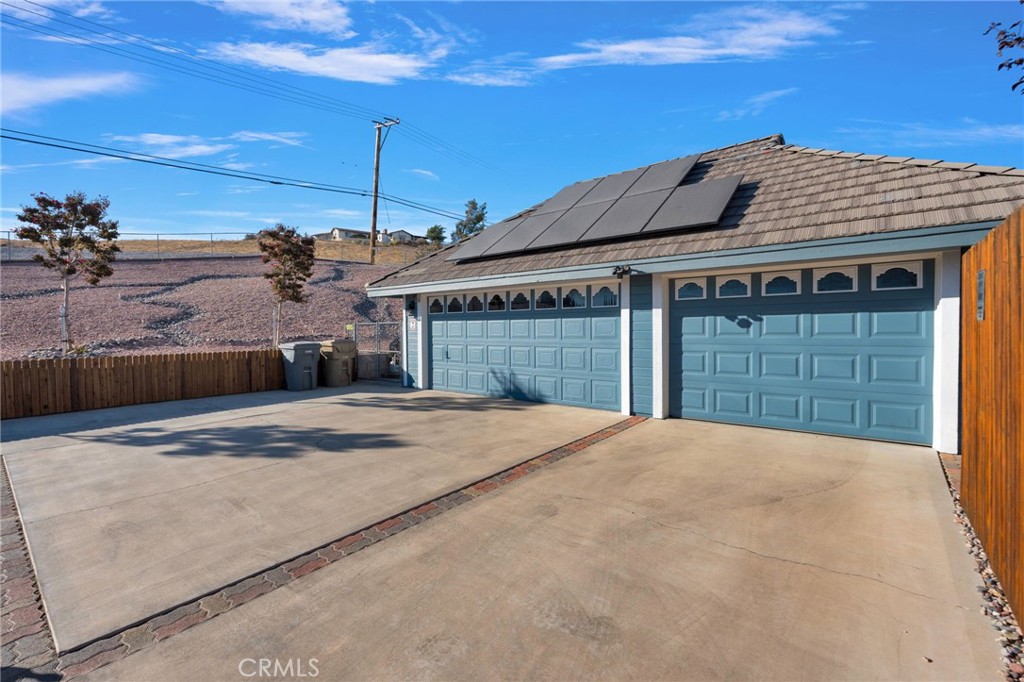 Home with two blue garage doors, rooftop solar panels, and a wide concrete driveway.