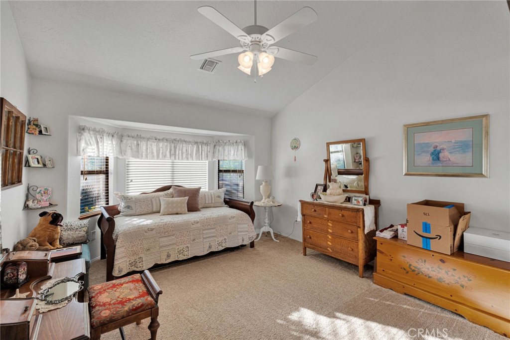 Furnished bedroom with a wide window, ceiling fan, beige carpet, and wooden dressers.