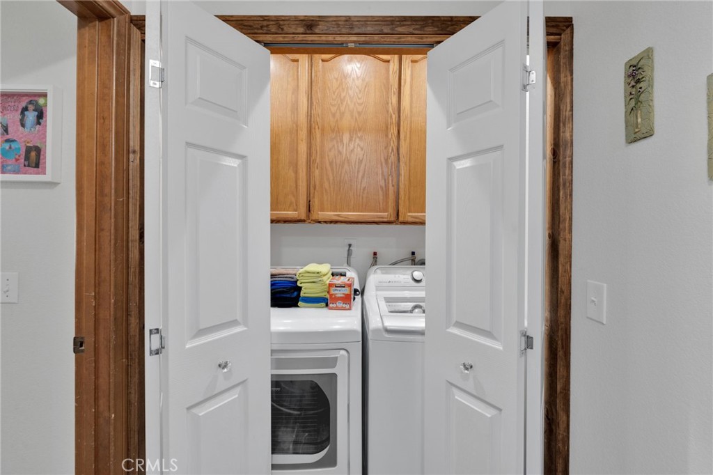 Laundry closet with washer and dryer beneath wood cabinets, viewed through open double doors.