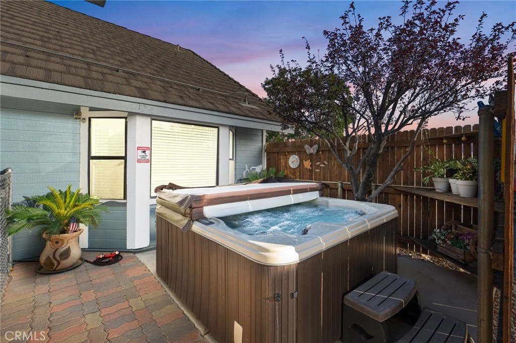 Backyard hot tub beside the house, enclosed by a wooden fence and shaded by a leafy tree.